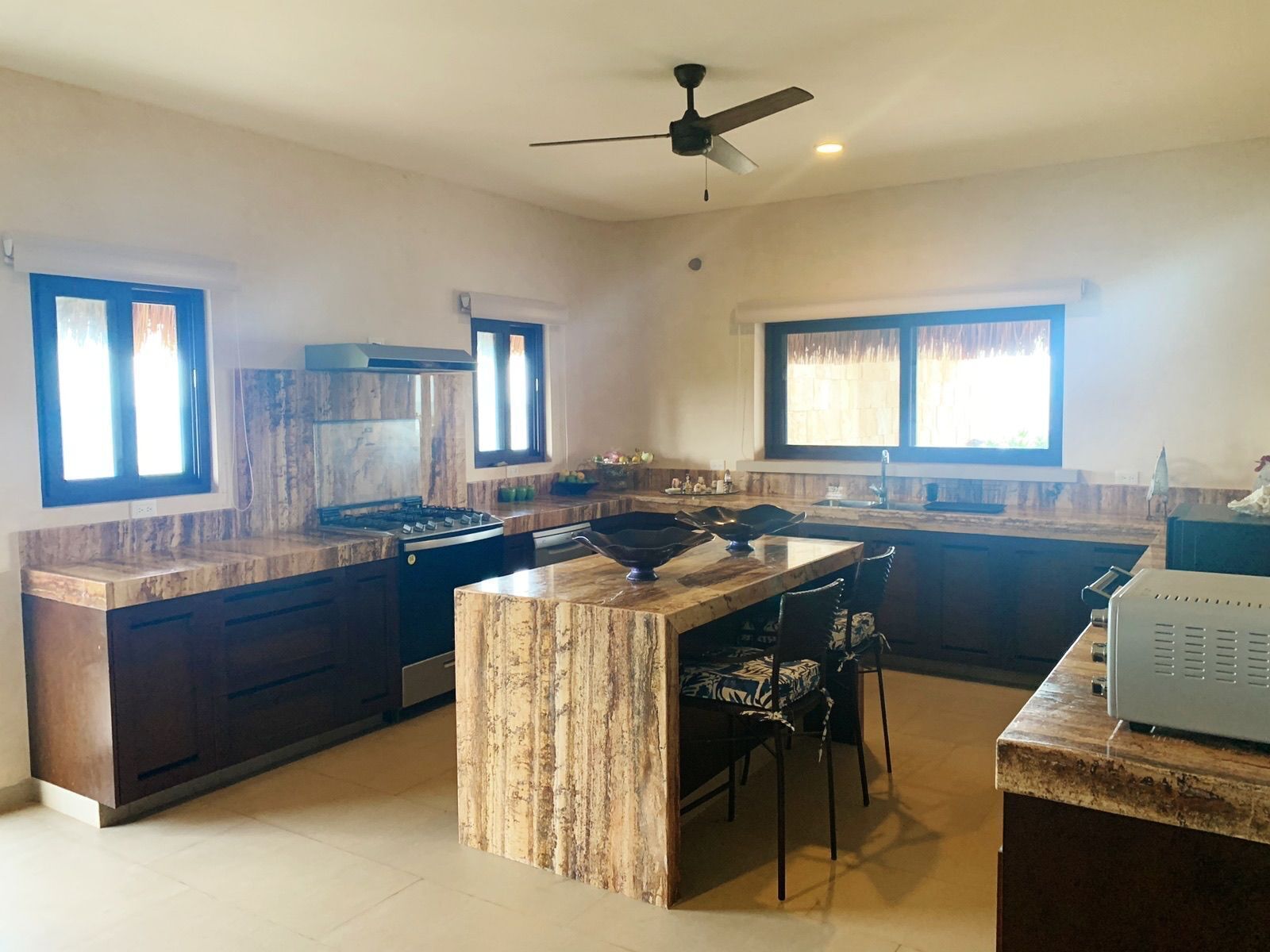 A modern kitchen with a central island, dark cabinetry, and a ceiling fan.