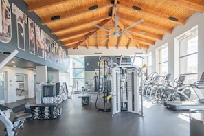 Un gimnasio con diversos equipos de ejercicio, incluyendo cintas de correr y máquinas de pesas, bajo un techo de madera con ventanas amplias.