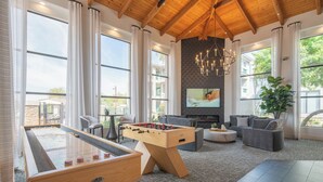 Ein geräumiges Wohnzimmer mit Tischfußball, bequemen Sitzgelegenheiten, einem Kamin und großen Fenstern mit Blick ins Freie.