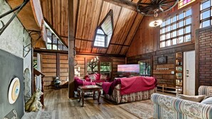 Il s'agit d'une pièce spacieuse de style loft, avec un plafond haut, des poutres en bois et une grande fenêtre. On y trouve un coin salon confortable avec des canapés à motifs et un téléviseur.