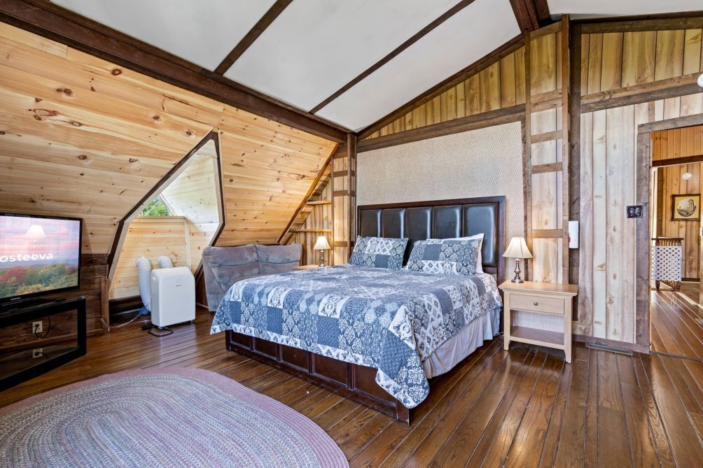 Une chambre confortable avec un plafond en bois, un grand lit avec une literie à motifs, une télévision et une petite table de chevet avec une lampe.