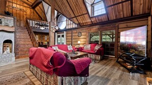 L’intérieur chaleureux d’un chalet en bois, avec une cheminée, un ensemble de canapés et une grande fenêtre donnant sur un paysage pittoresque.