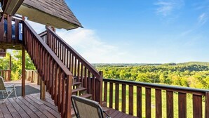 Une terrasse en bois avec un escalier menant à une zone abritée, d’où l’on peut admirer un paysage boisé.
