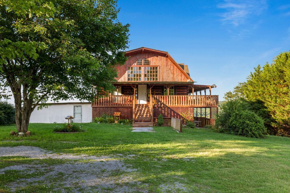 Une grande maison en bois avec un porche, une véranda couverte à l’avant et un petit jardin devant.