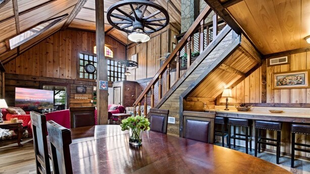 Un intérieur spacieux en bois, avec une grande table à manger, un escalier et un coin bar.