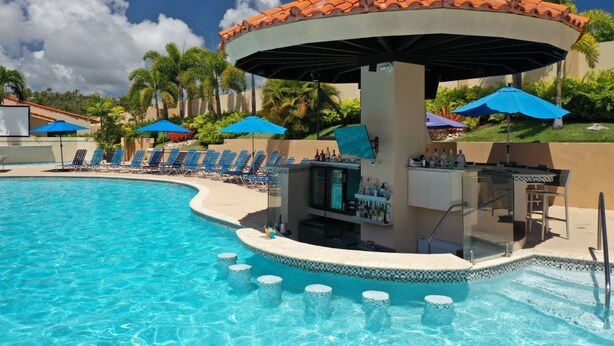 A pool area with a bar, lounge chairs, and umbrellas.