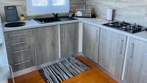 Kompakti keittiö, jossa on harmaat kaapit, musta pesuallas, liesi ja ikkuna, jossa on verhot.