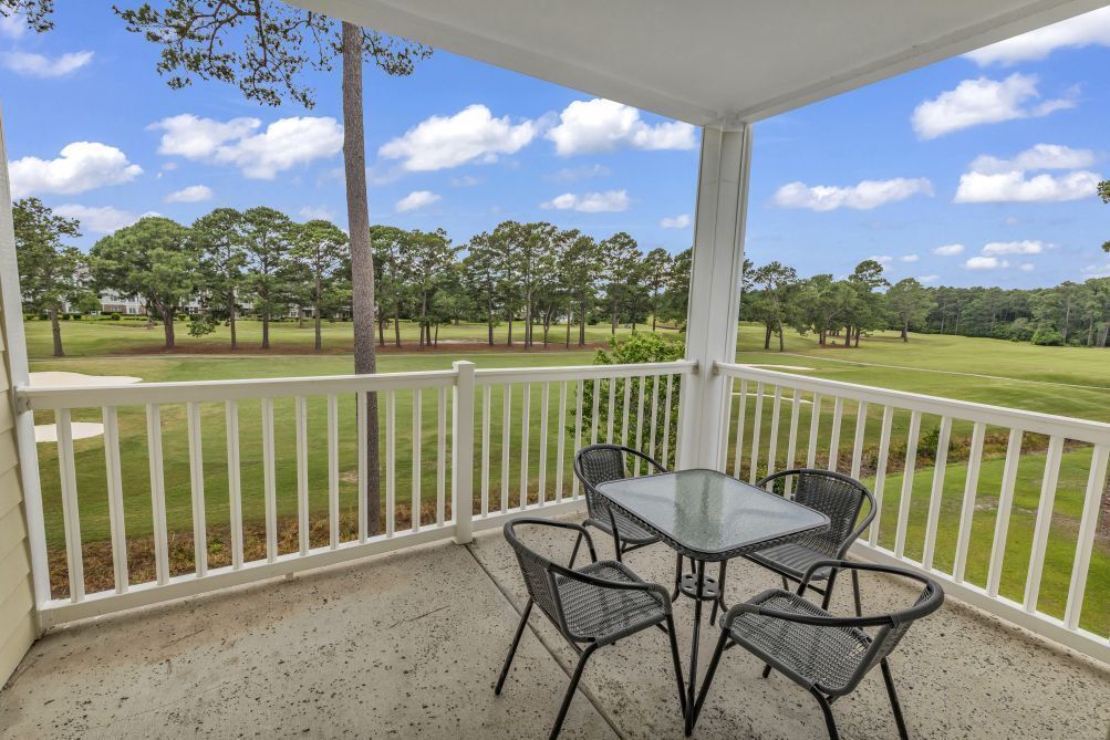A covered patio with a table and chairs, overlooking a well-maintained lawn and trees.