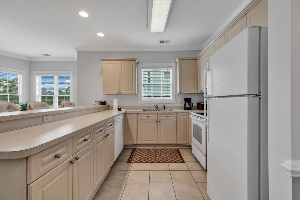 A modern kitchen with light wood cabinets, a white refrigerator, and a built-in oven.