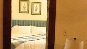 A hotel room with a checkered bedspread, a wooden nightstand with a lamp, and a hallway leading to another room. - The Stone room Suite #11, sleeps 5 guest (Hot Springs)
