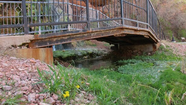 A metal bridge over a small stream with surrounding greenery and rocks. - The Stone room Suite #11, sleeps 5 guest (Hot Springs)