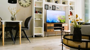 A living room with a television, a bookshelf, a dining table with chairs, and a vase with flowers. - Appartment (2 rooms / 4 persons) with terrasse and swimminpool (Fréjus)