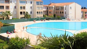 A swimming pool surrounded by multi-story buildings with balconies, a clear sky, and greenery. - Appartment (2 rooms / 4 persons) with terrasse and swimminpool (Fréjus)
