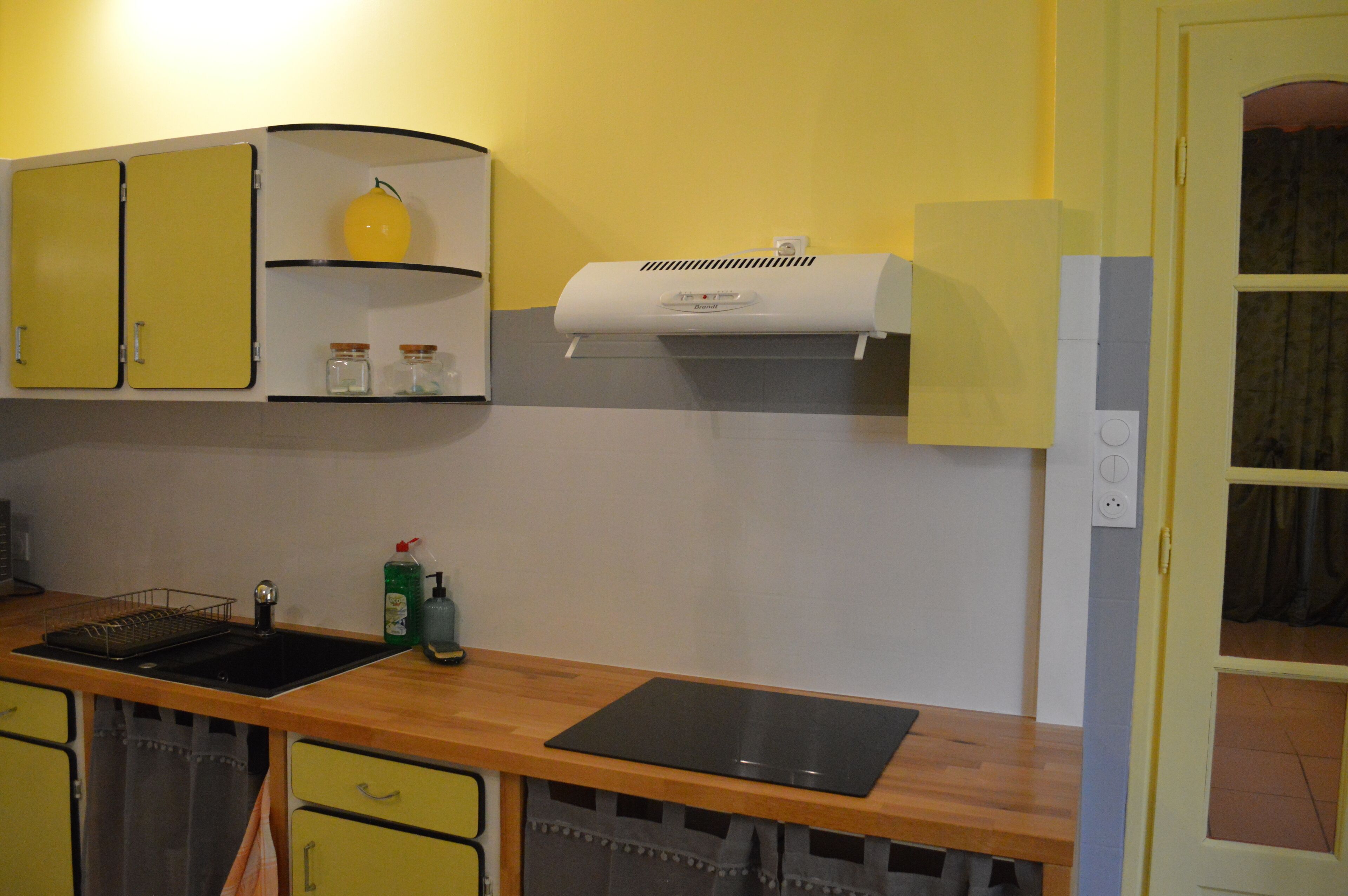 Une cuisine avec des meubles de couleur jaune, un plan de travail noir et un climatiseur blanc.