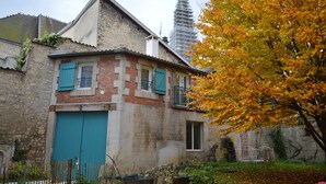 A two-story building with a brick facade, a blue shuttered door, and a balcony with a metal railing. - Gîte La Rose Trémière - Maison Avec Terrasse, Idéale Pour un Séjour en Famille (Joinville)