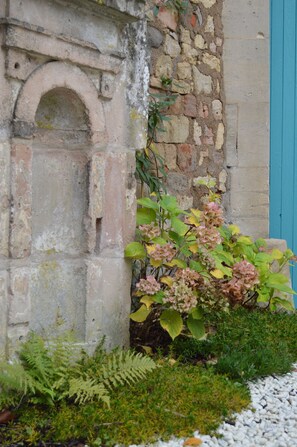 A stone wall with a small archway and a plant with pink flowers growing against it. - Gîte La Rose Trémière - Maison Avec Terrasse, Idéale Pour un Séjour en Famille (Joinville)