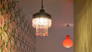 A room with a patterned wallpaper, a wooden bed with pillows, a small stool, a patterned rug, and a chandelier. - Gîte La Rose Trémière - Maison Avec Terrasse, Idéale Pour un Séjour en Famille (Joinville)