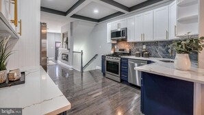 Una cucina moderna con mobili bianchi, piano cottura in acciaio inossidabile e un ripiano in marmo.