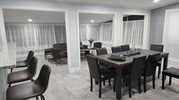 A modern dining area with a large table and chairs, a sofa, and a small side table with a plant.