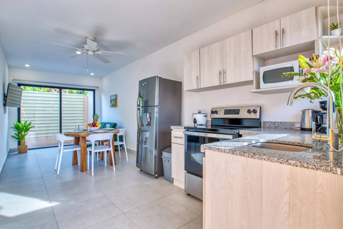 A modern kitchen with a stainless steel refrigerator, a microwave, and a stove. There is a dining area with a table and chairs.