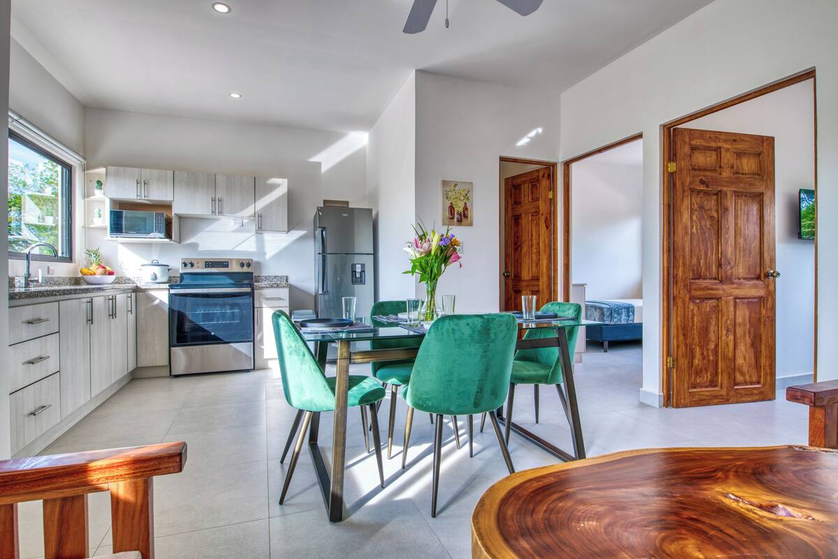 A modern kitchen with stainless steel appliances, a dining area with green chairs, and a wooden dining table.