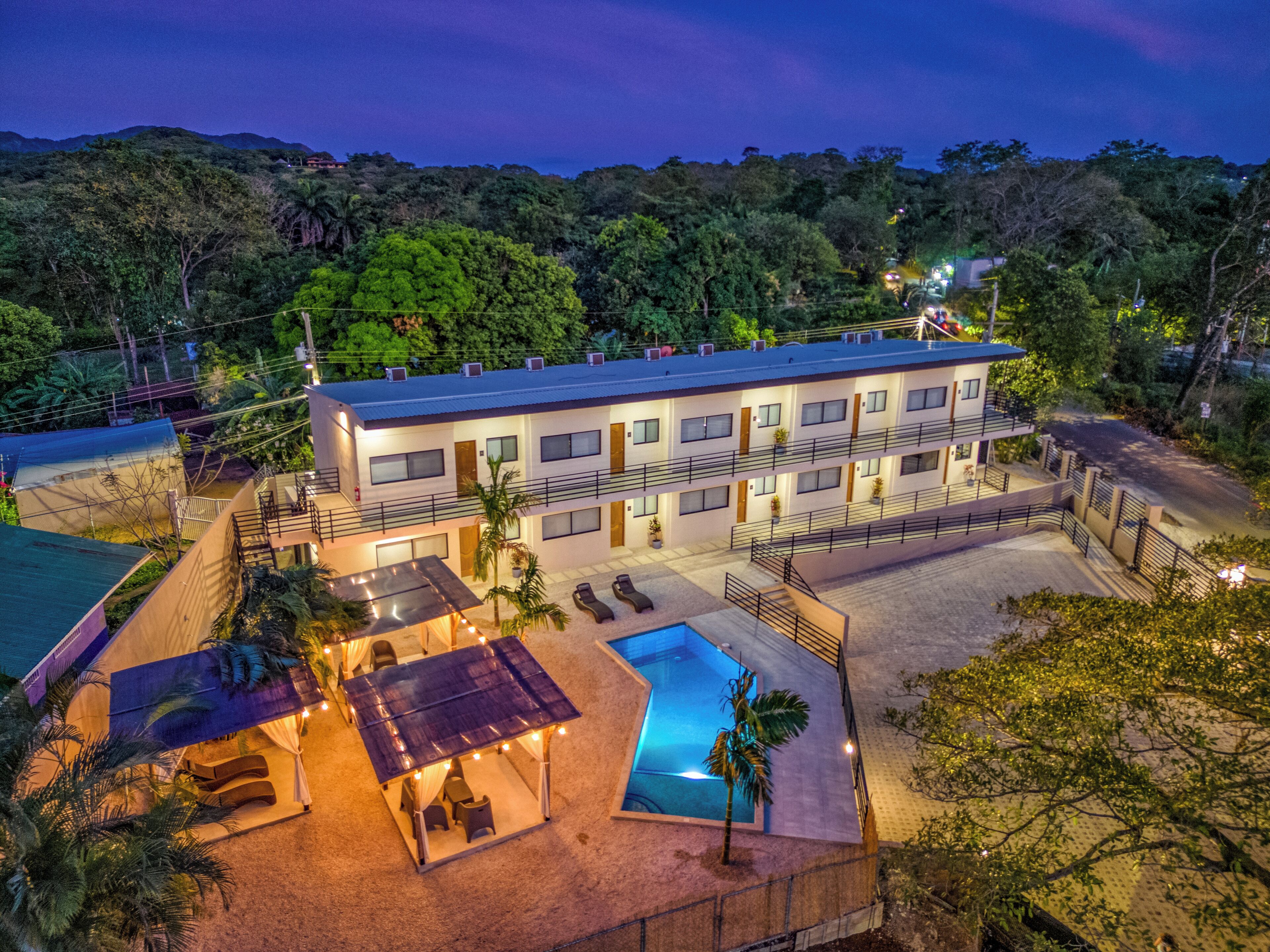 A multi-story hotel with a swimming pool, outdoor seating, and a view of the surrounding forest.