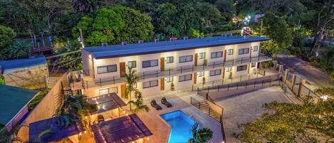 A multi-story hotel with a swimming pool, outdoor seating, and a view of the surrounding forest.