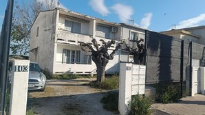 A two-story building with a gated entrance, a car parked in front, and a tree with lion sculptures.