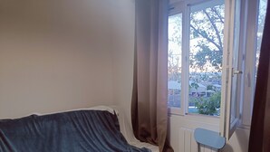 A small room with a single bed, a window, and a chair.