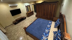 Ein Schlafzimmer mit einem großen Bett, einem Kleiderschrank, einem Fernseher und einem Spiegel.