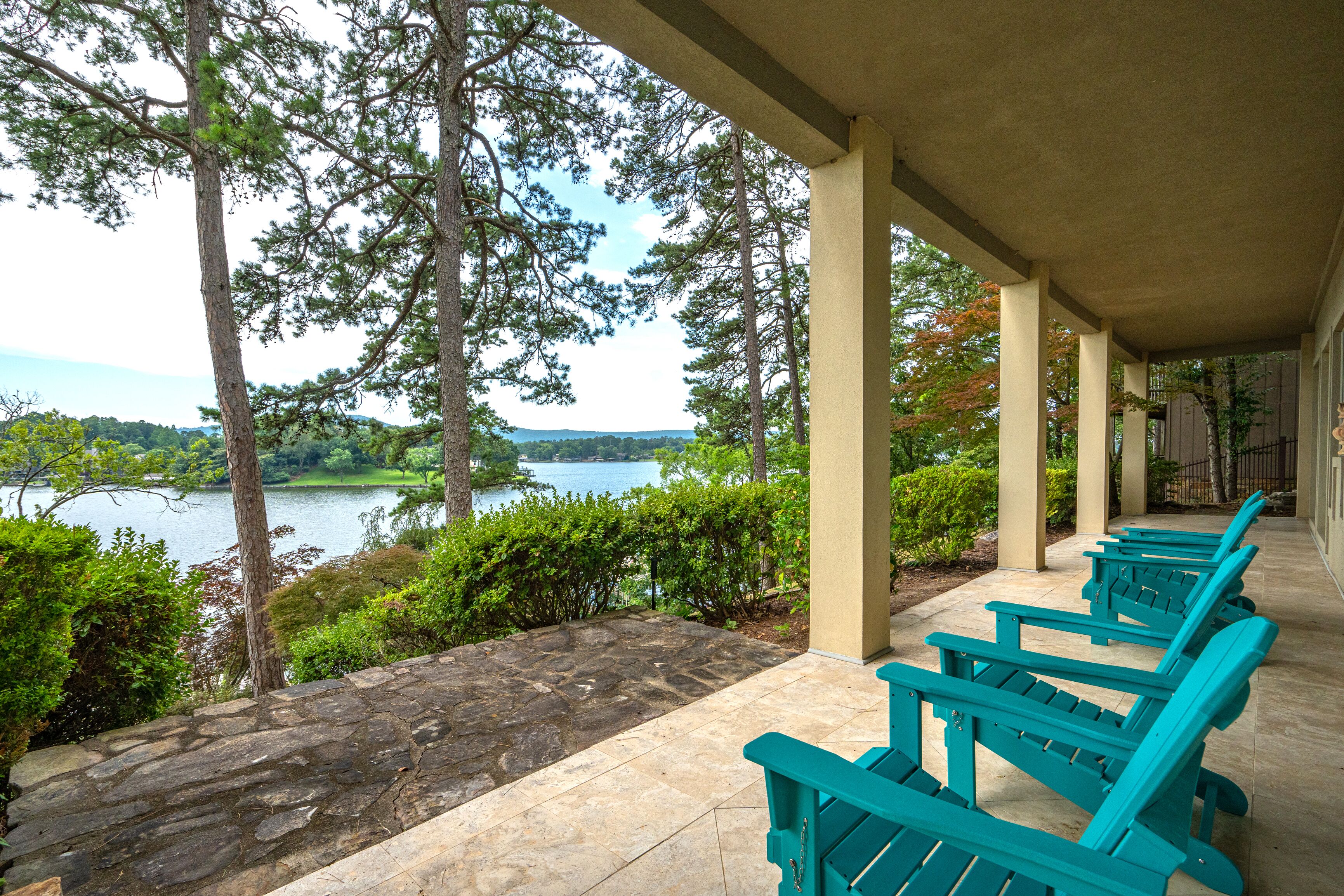 A covered outdoor seating area with chairs overlooking a lake and trees.
