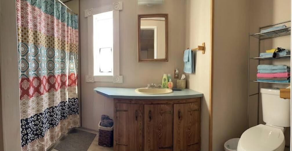 A bathroom with a wooden vanity, a sink, a mirror, and a toilet.
