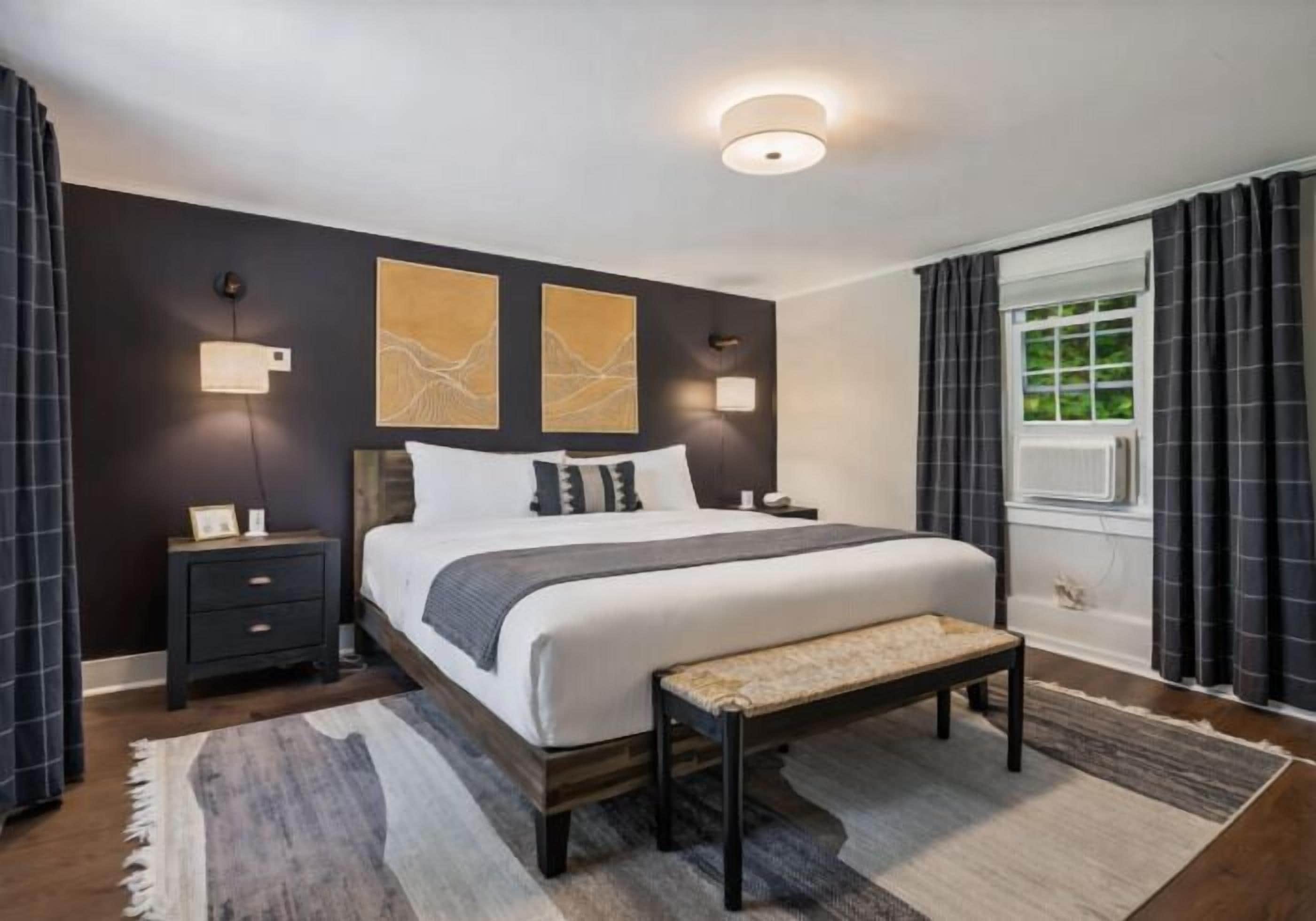 A modern bedroom with a large bed, bedside tables, a bench, and artwork on the wall.