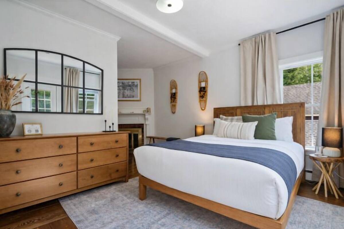 A bedroom with a bed, dresser, bedside table, and a window with curtains.