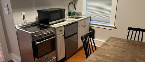 A compact kitchen with a stove, microwave, sink, and a dining table.