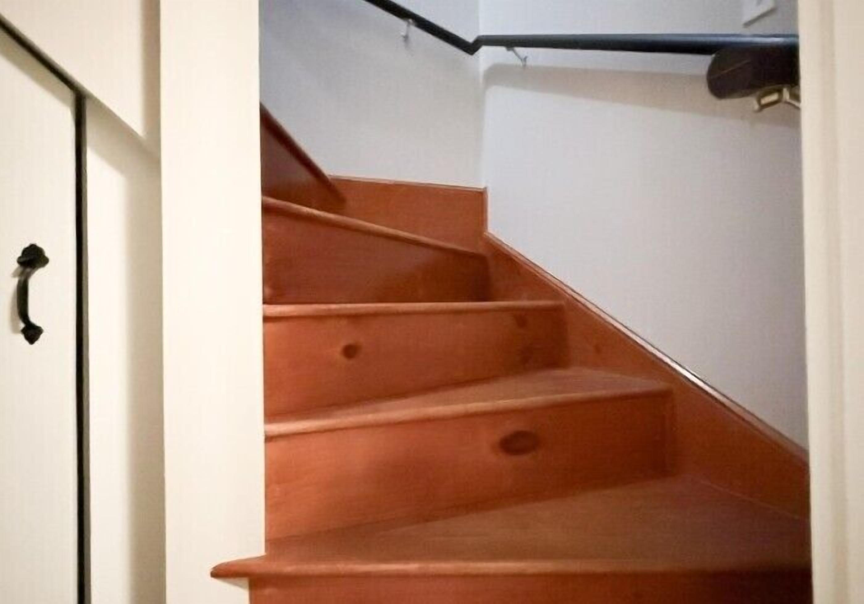 A staircase with wooden steps and a black handrail, leading to a white wall.