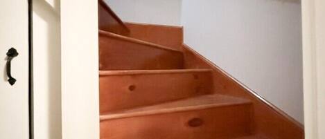 A staircase with wooden steps and a black handrail, leading to a white wall.