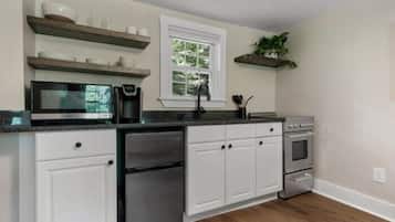 A kitchen with white cabinets, a microwave, a dishwasher, an oven, and a window with a view of trees.