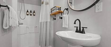 A bathroom with a shower, a sink, a mirror, and a towel rack.