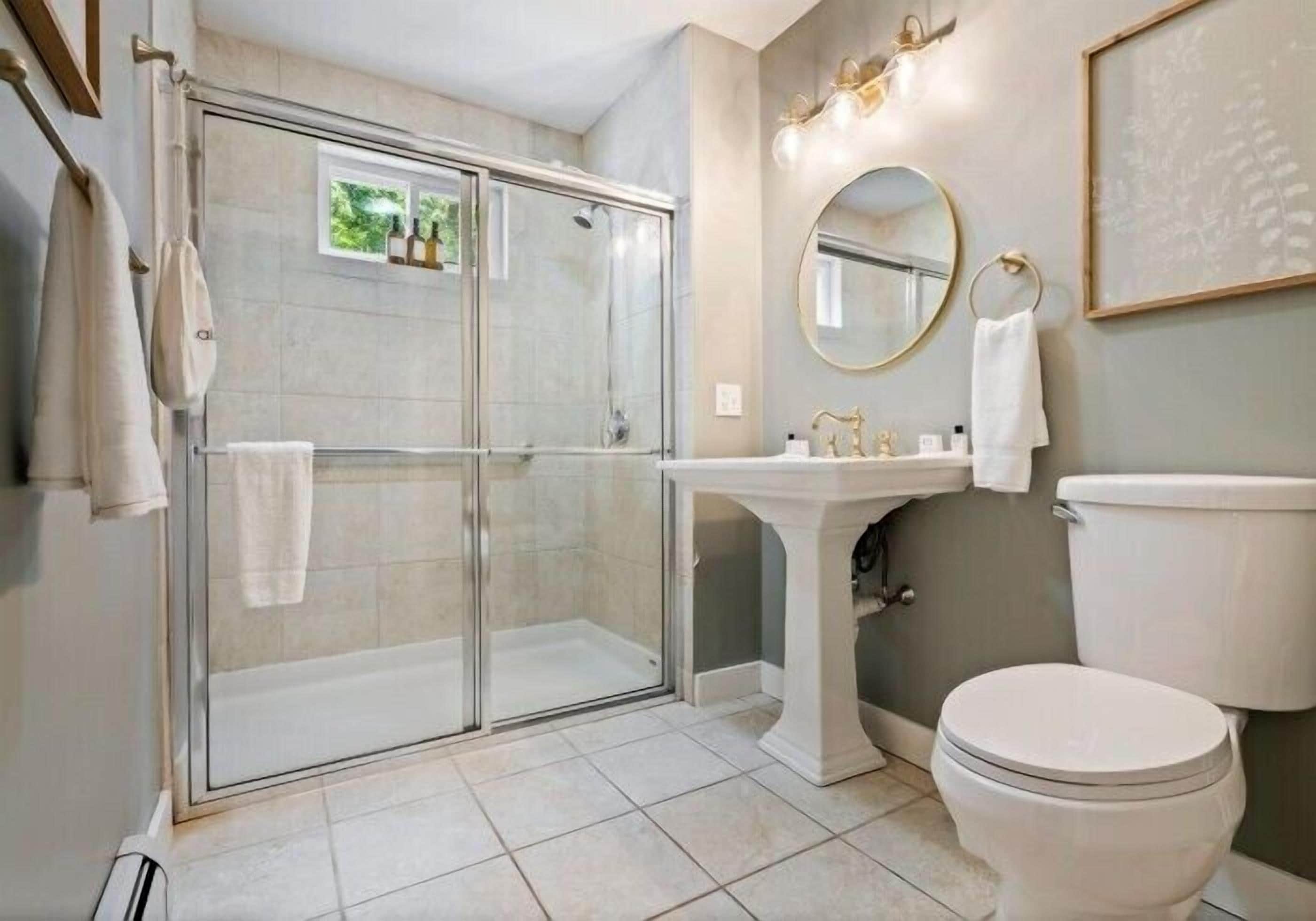 A bathroom with a glass-enclosed shower, a pedestal sink, a toilet, and a wall-mounted mirror.