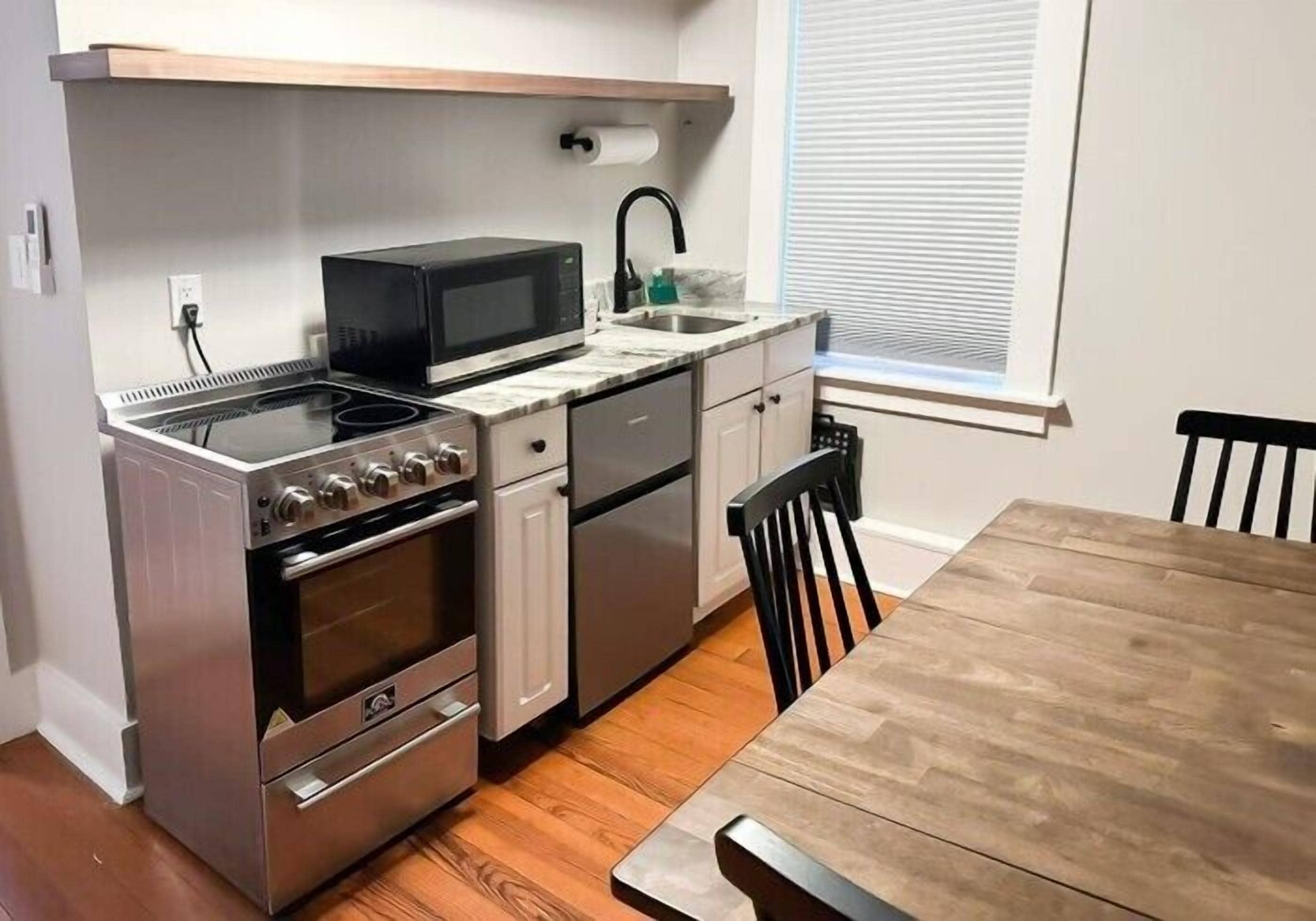 A compact kitchen with a stove, microwave, sink, and a dining table.