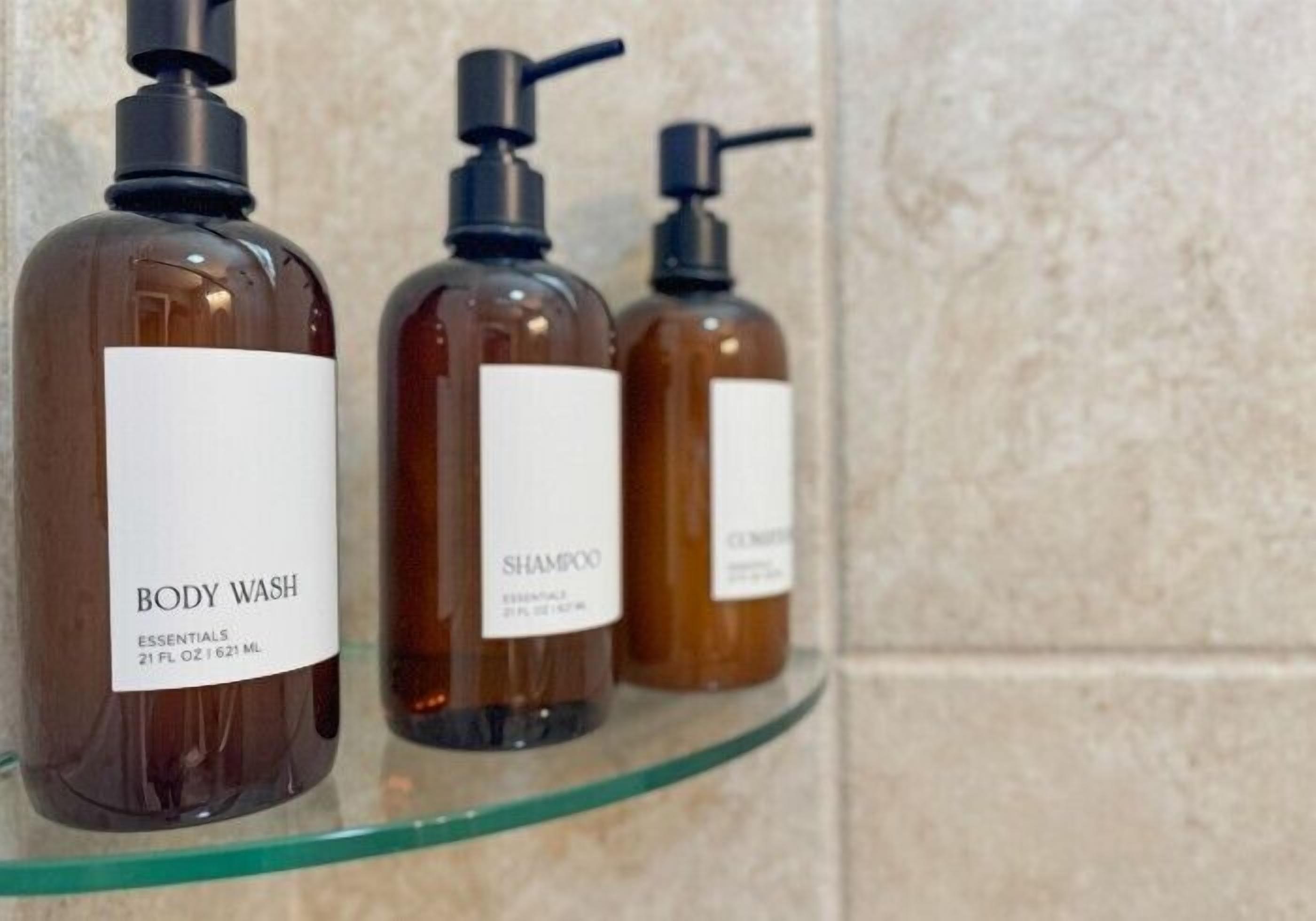 Trois bouteilles de gel douche et de shampoing sont posées sur une étagère en verre.
