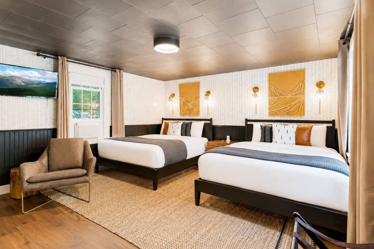 A hotel room with two beds, a sofa, a TV, and artwork on the walls.