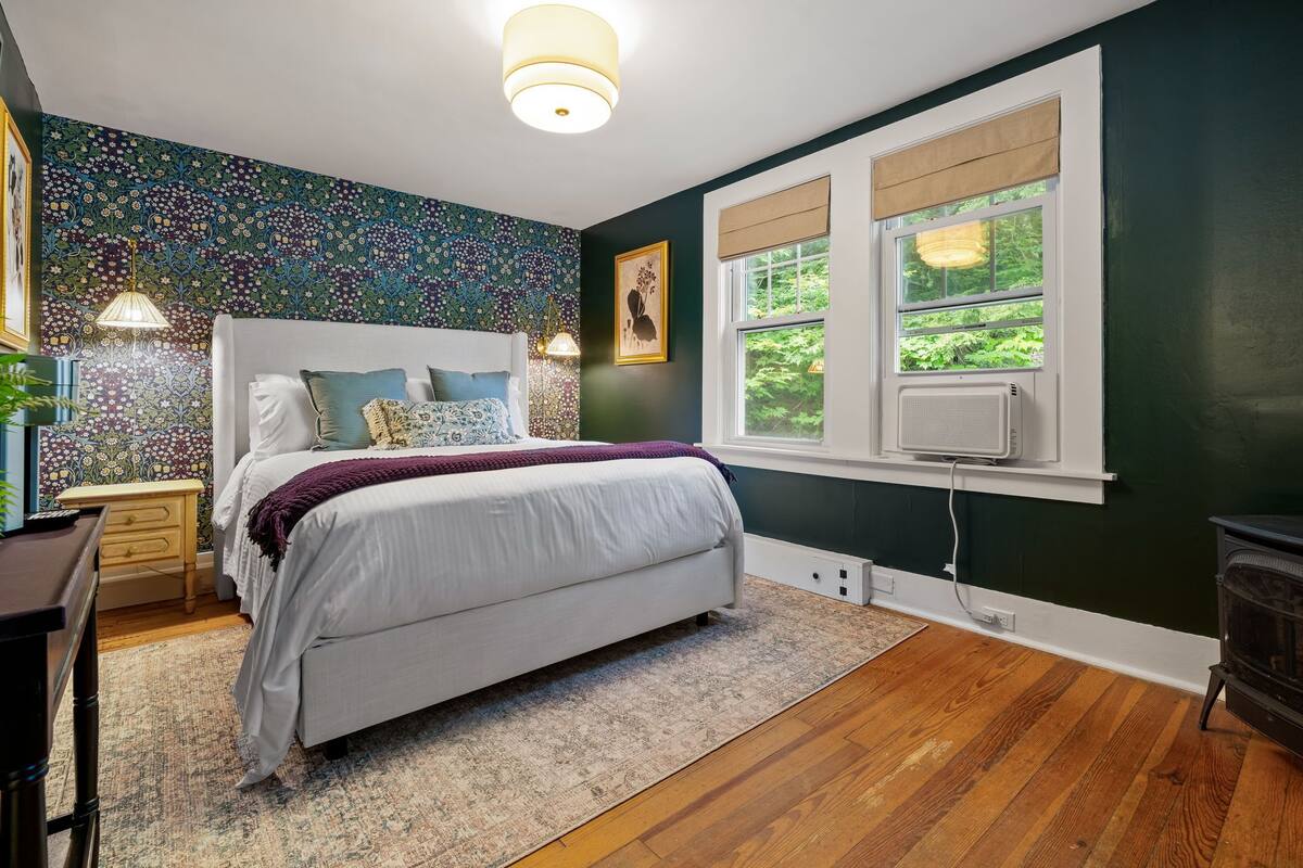 A bedroom with a bed, bedside tables, a nightstand, a window with a view, and a wall with a floral pattern.