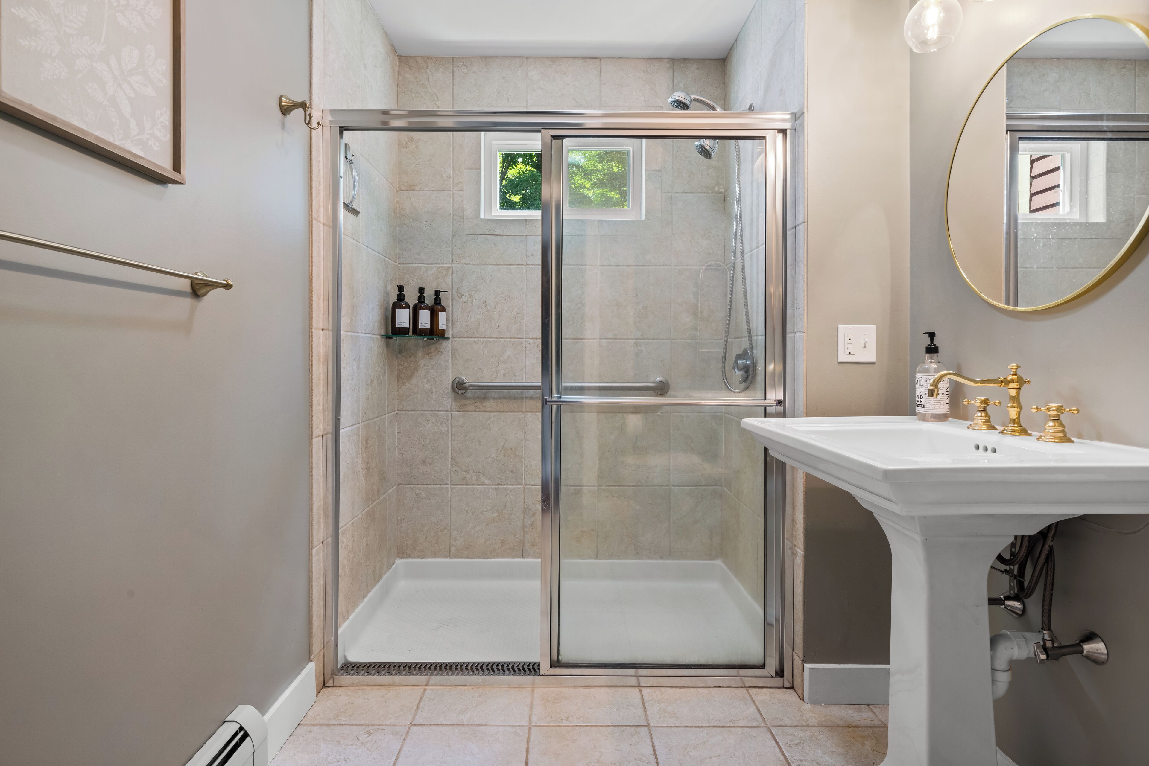 A modern bathroom with a glass-enclosed shower, a white sink with gold fixtures, and a framed picture on the wall.