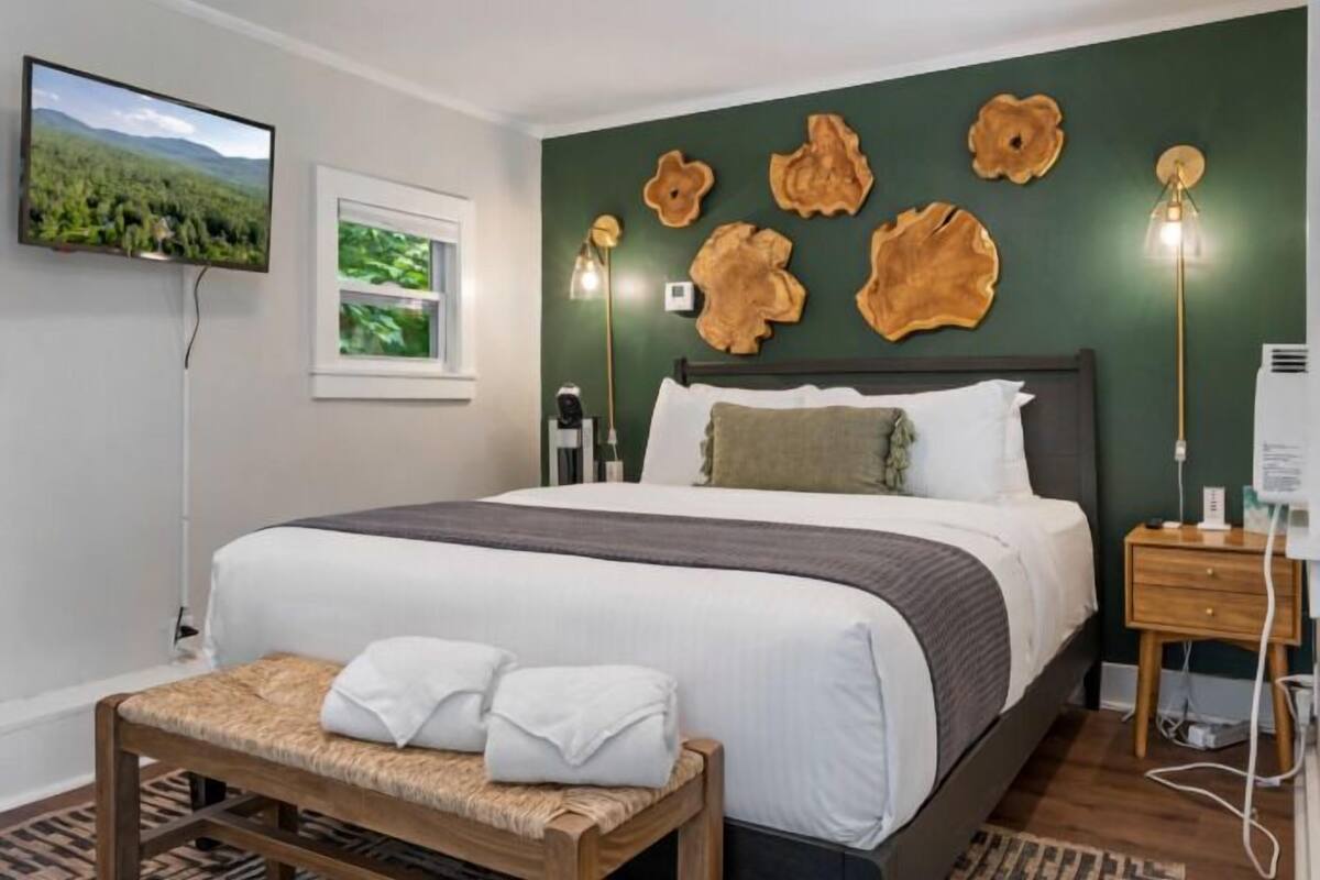 A neatly arranged bedroom with a bed, bedside table, lamp, and a television on the wall.