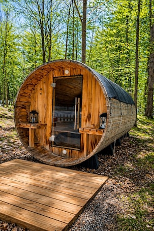 A wooden barrel-shaped cabin with a wooden deck leading to the entrance, surrounded by a forest.. The Aurora Inn & Cottages