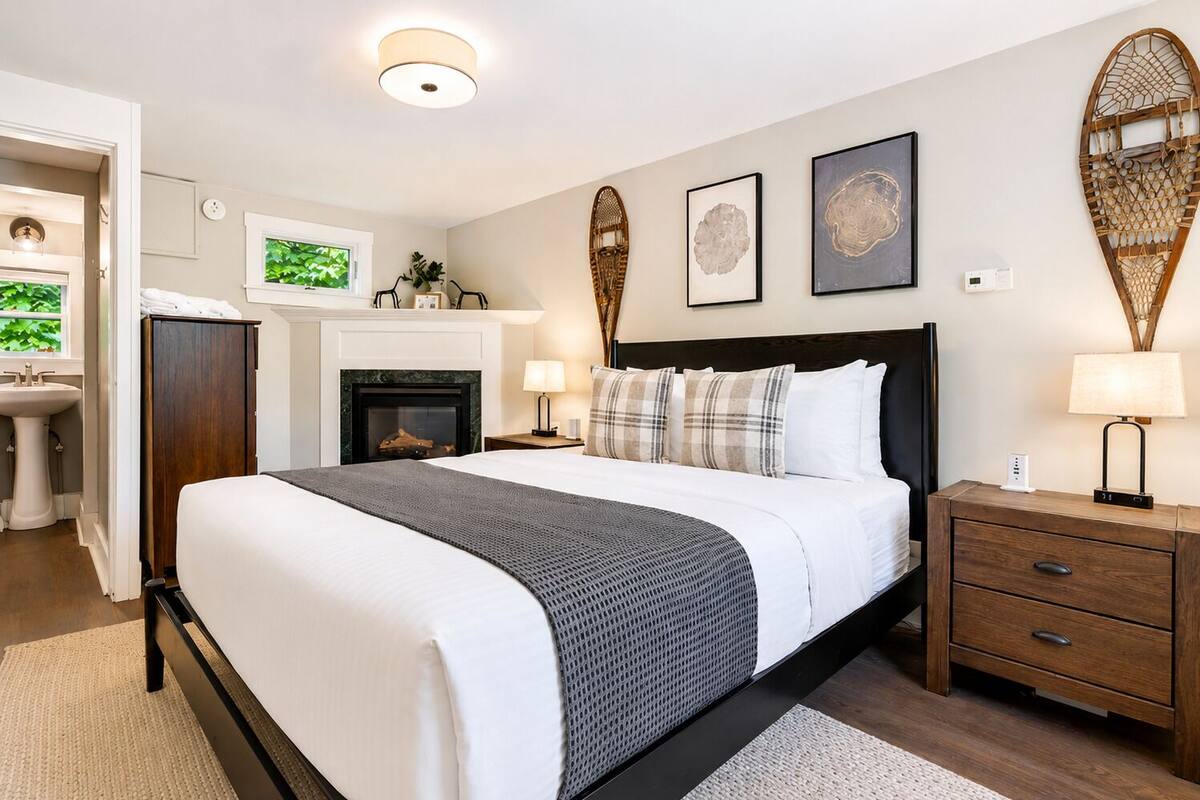 A bedroom with a bed, bedside tables, a fireplace, and wall art.