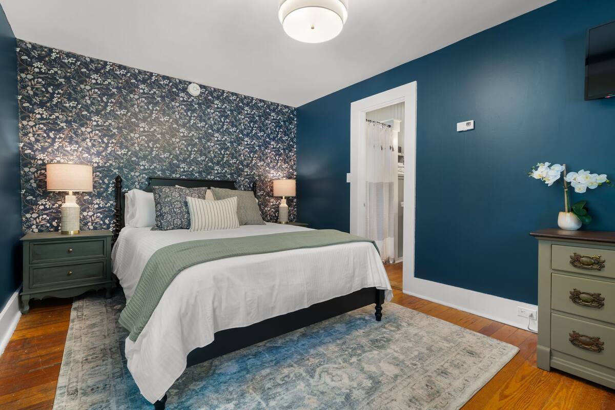 A bedroom with a bed, nightstands, a dresser, and a wall with floral wallpaper.