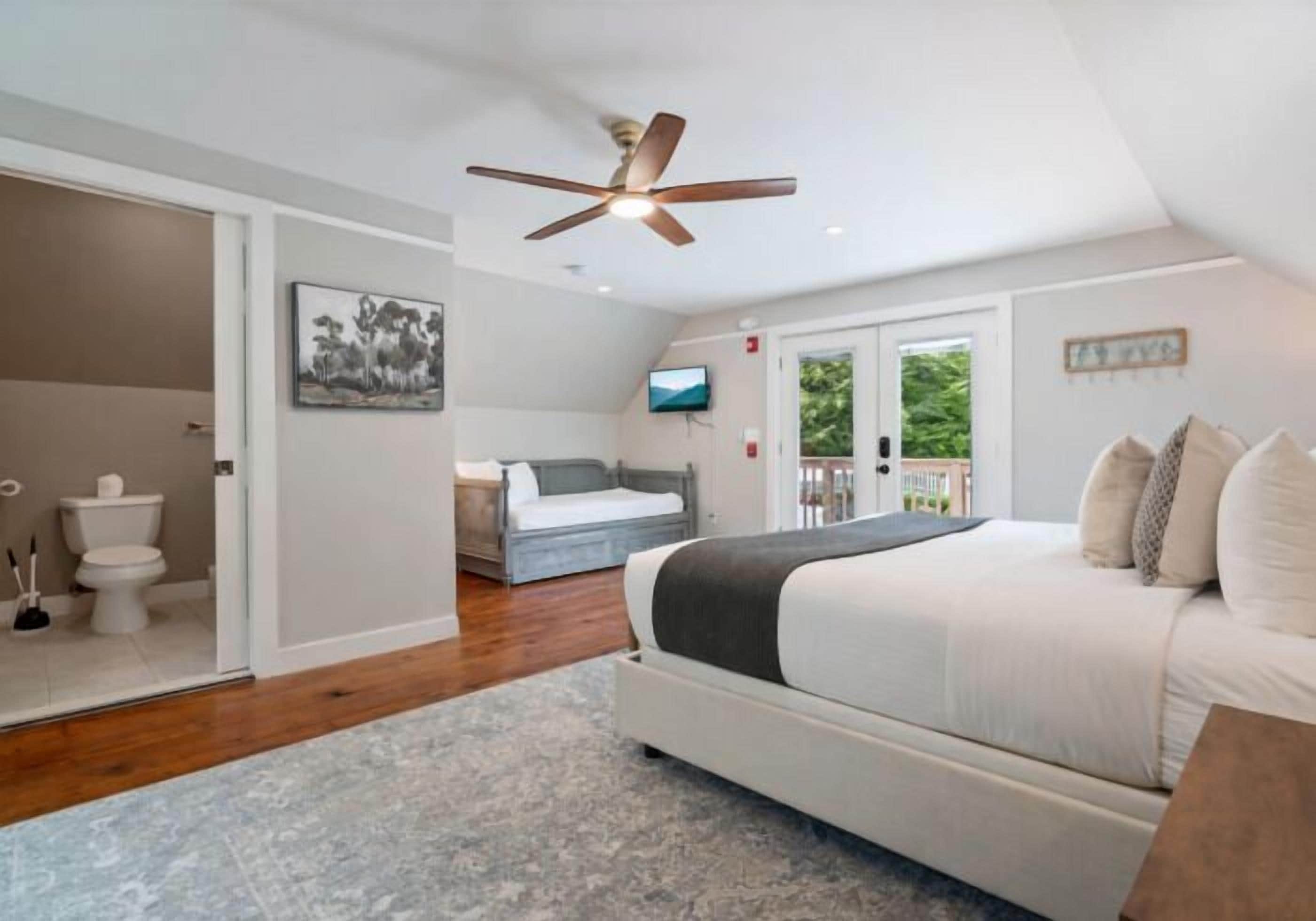 A bedroom with a bed, a ceiling fan, a TV, and a view of the outdoors.